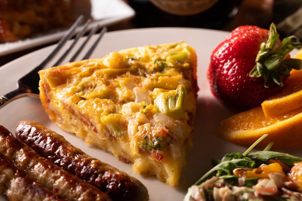 Breakfast quiche, sausages, and fruit on white china plate. Start your day with a delicious gourmet meal at our Michigan Bed and Breakfast.