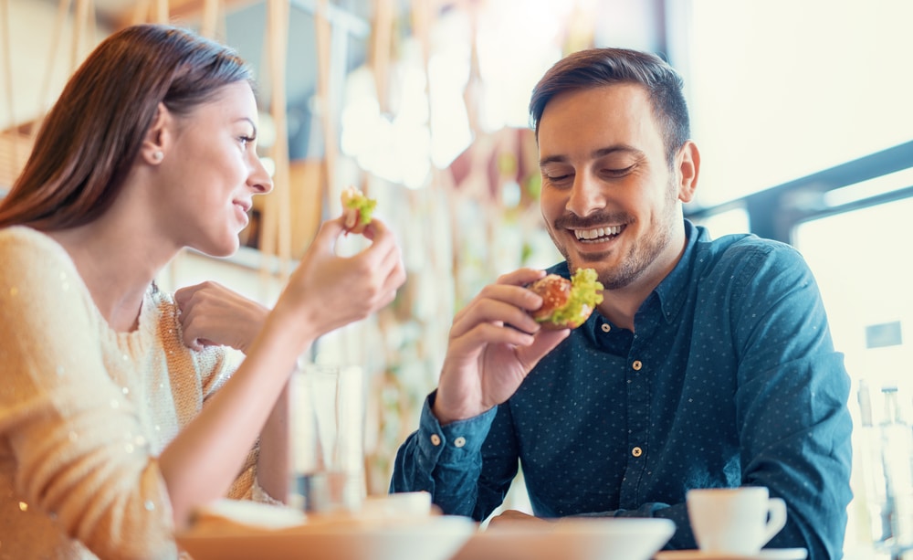 happy couple eating sandwiches in a sunny restaurant