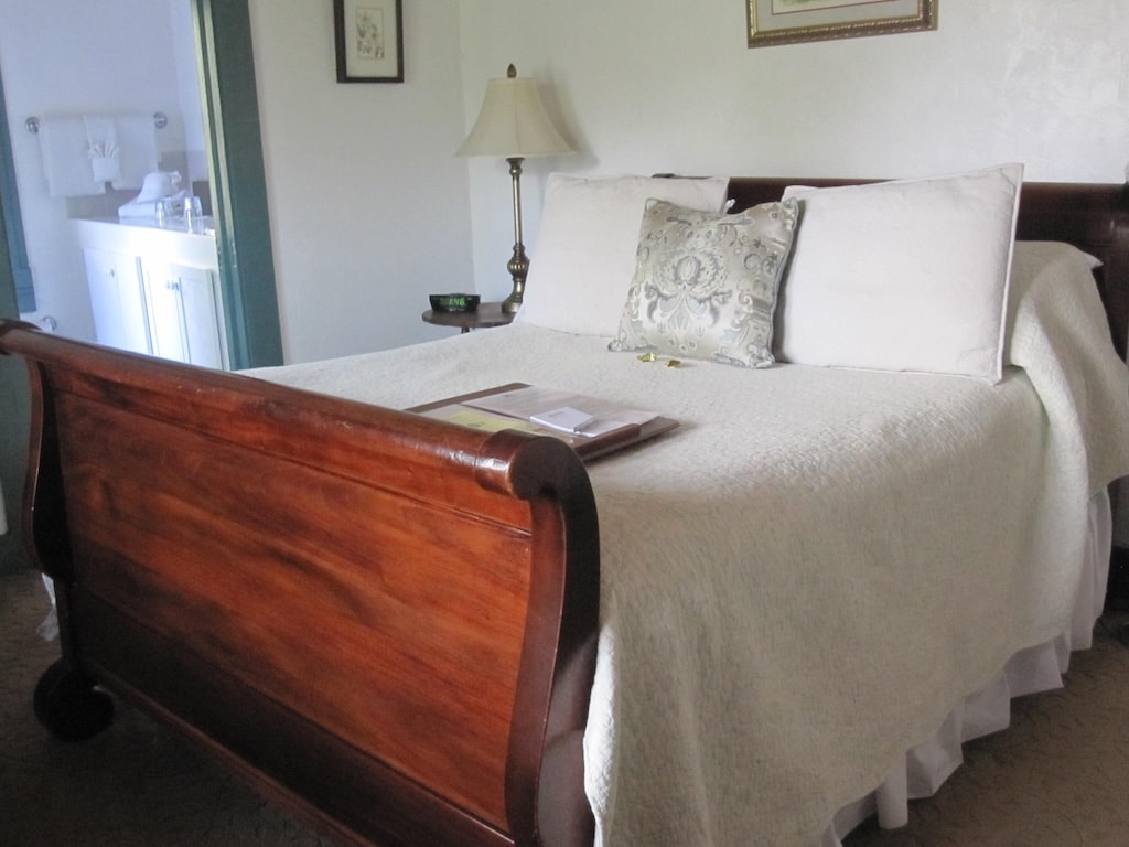 Stay at the Best Bed and Breakfast in St. Augustine. Image of sleigh bed and white comforter with modern bathroom in the background.