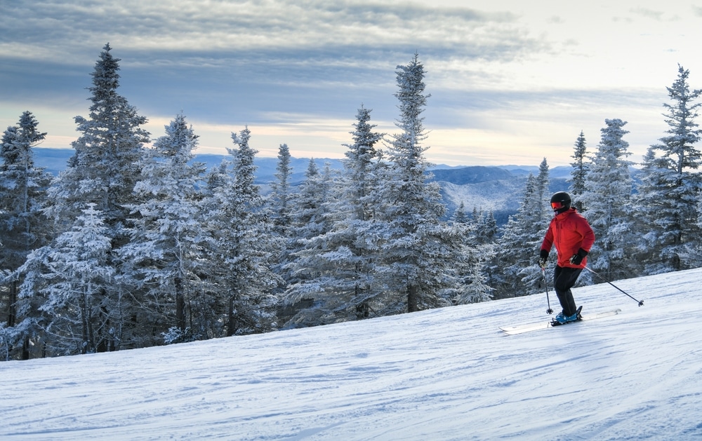Enjoy any one of the best New Hampshire ski resorts. Man in a red jacket skies downhill.