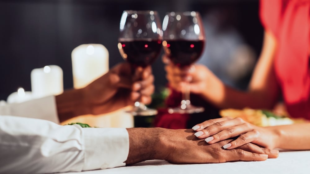 Enjoy a glass of wine during one of the best romantic spa getaways and The Orchard Inn and Spa. A couple holding hands and glasses of red wine.