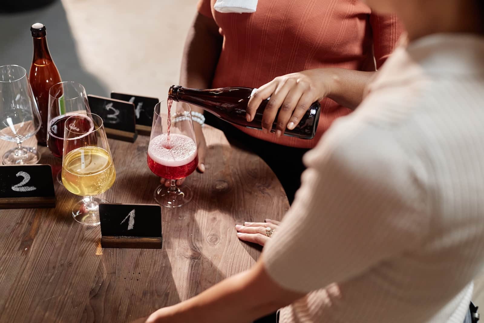 High angle shot of female African American sommelier pouring craft berry cider into glass during product sampling in tasting room near Finger Lake Cider House
