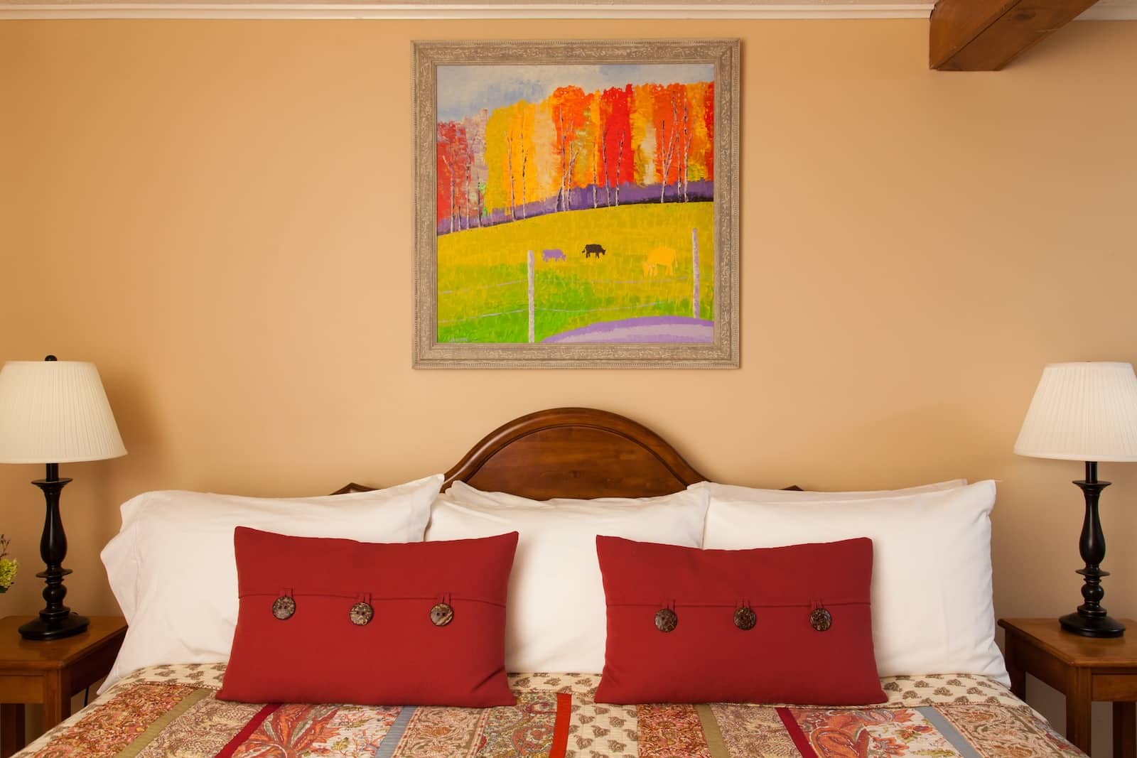 Stay at our New Hampshire Bed and Breakfast. Here is a king sized bed with red pillows and colorful artwork hanging over the bed. 