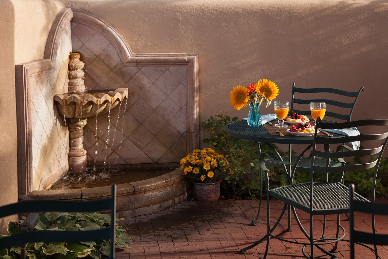 Breakfast for two on a peaceful patio at a Bed and Breakfast in Santa Fe, featuring a table beside a flowing water feature and elegant Southwestern surroundings.