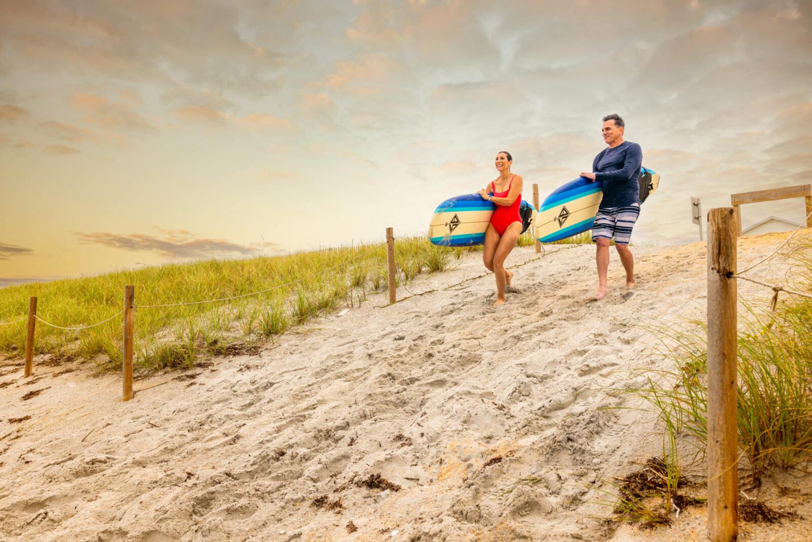 Couple walks our private beach walkover with surfboards. The water is still pleasant in Fall in Florida