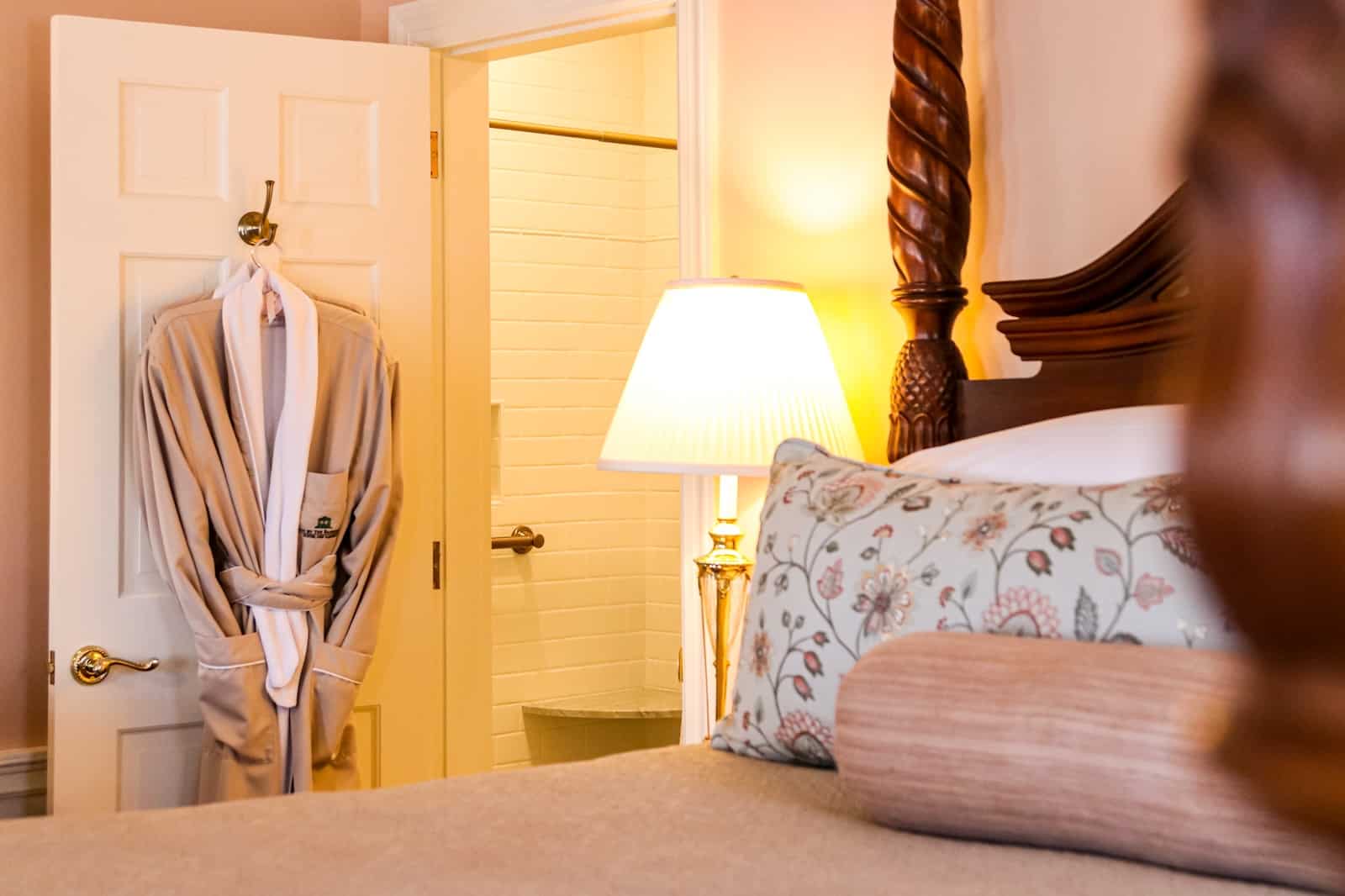 A room at one of the best hotels in New Hampshire, Inn By the Bandstand, showcasing plush bedding, throw pillows, a lamp, and a robe in the background.