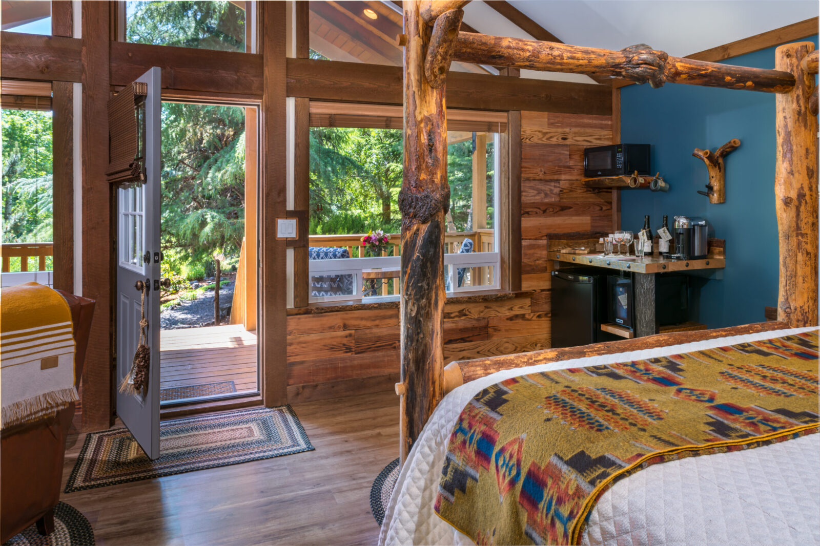 Mt Adams cabin at Carson Ridge Luxury Cabins with rough hewn wood bed frame, large windows, and small kitchenette.