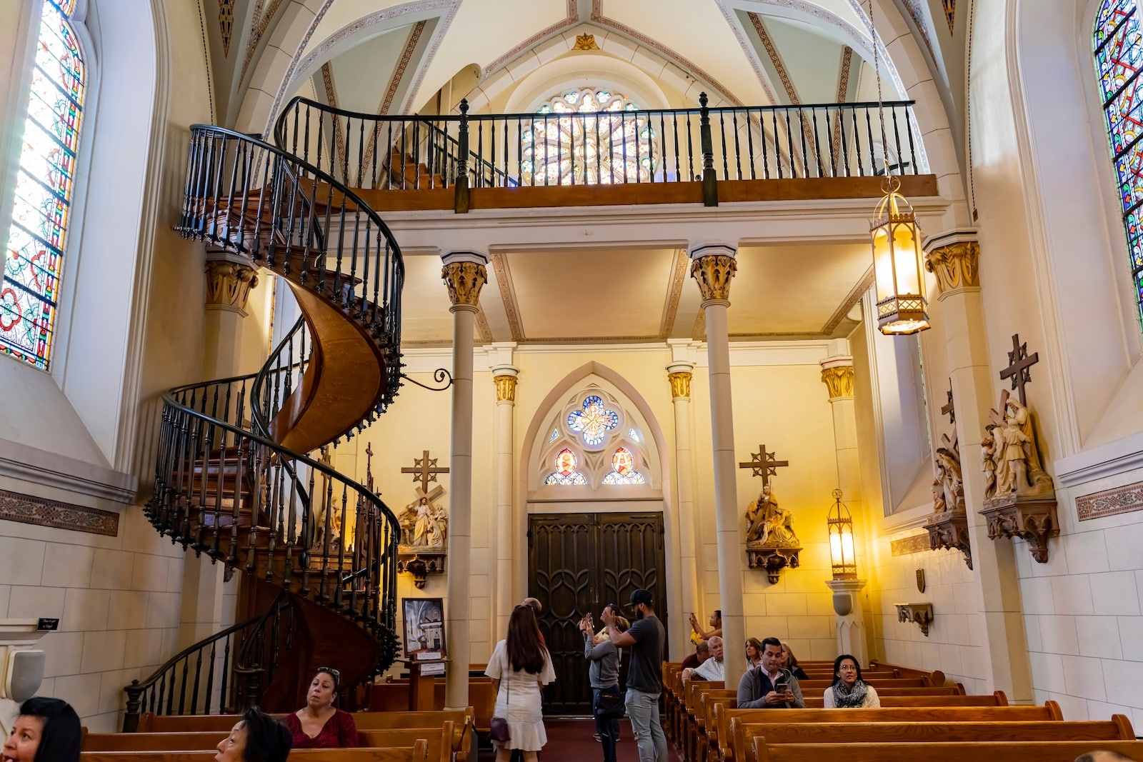 Visitors admire the famous Loretto Chapel Staircase inside the historic Loretto Chapel in Santa Fe, New Mexico, surrounded by Gothic architecture and stained glass details.