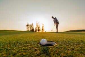Ball about to go into hole at Wisp Resort Golf, golfer in background on green at sunset.