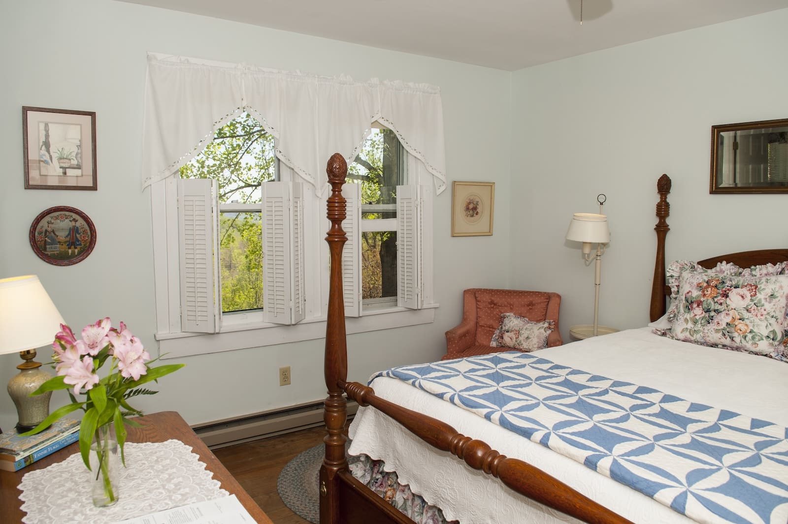 At the best Bed and Breakfast in Saluda, NC, you'll find accomodations like this one, featuring a comfy bed with a quilt, a dresser with fresh flowers on top, and a chair by the window.