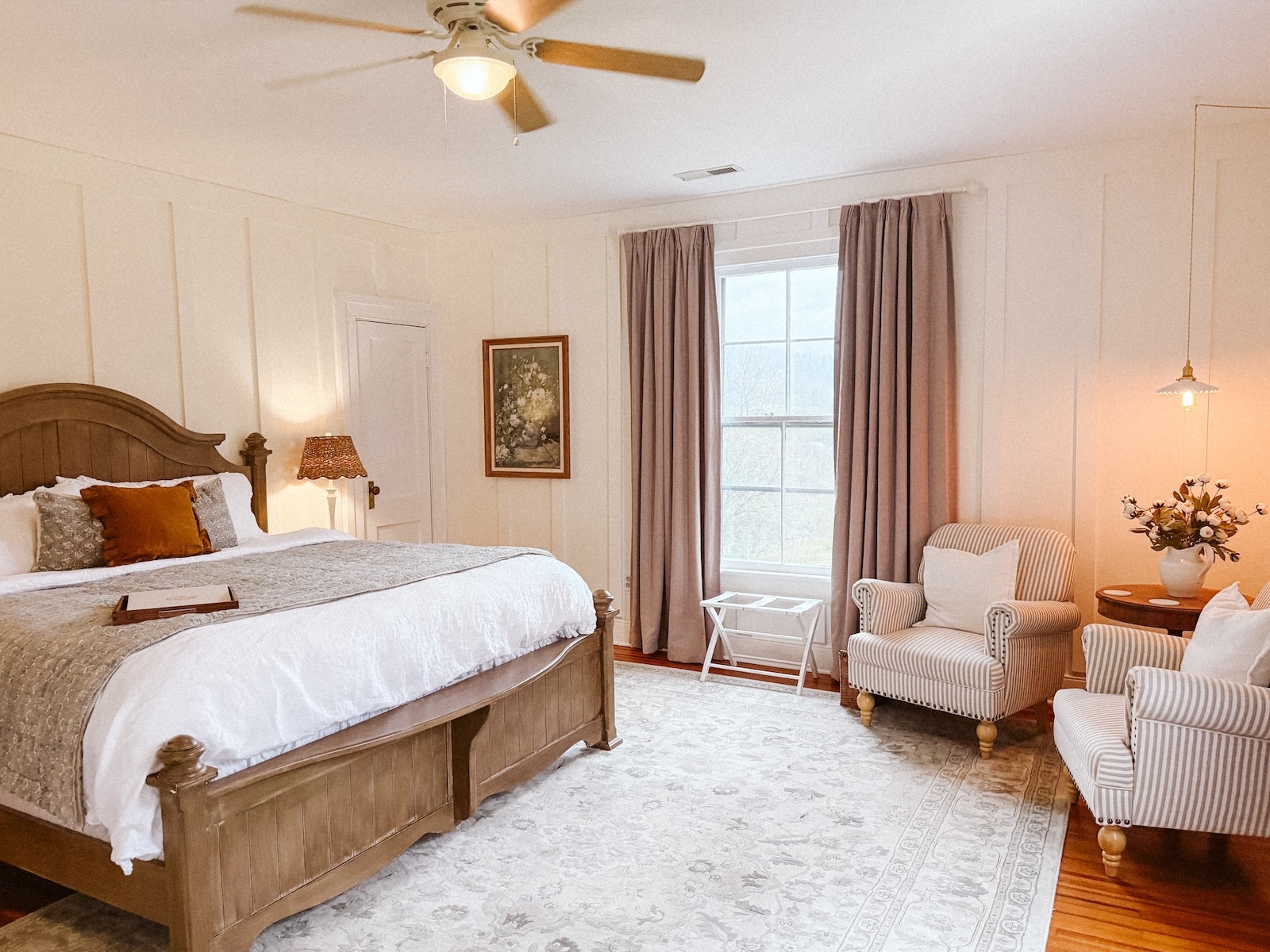 At a bed and breakfast Charlottesville VA, you'll find a spacious room complete with a king-size bed, rug, artwork, a window and two chairs for lounging.
