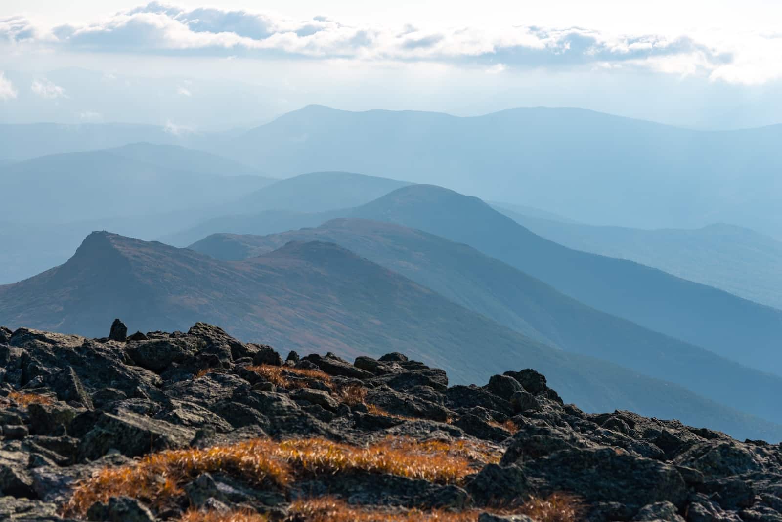 Rocks with blue mountains in the background showcasing hikes in the Presidential Range in New Hampshire.