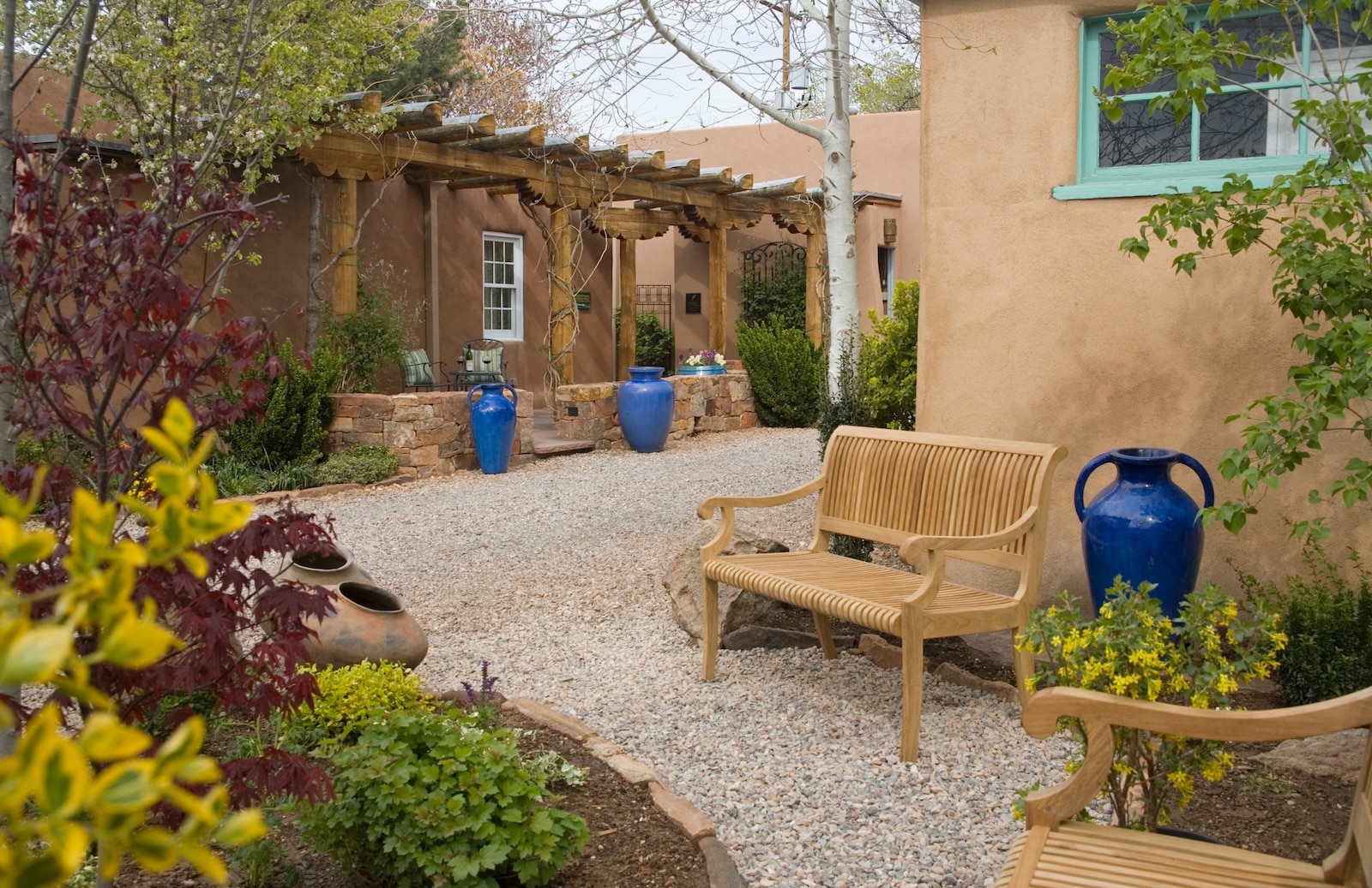 The gardens at El Farolito, a Santa Fe bed and breakfast, featuring plants, blue vases, and benches.