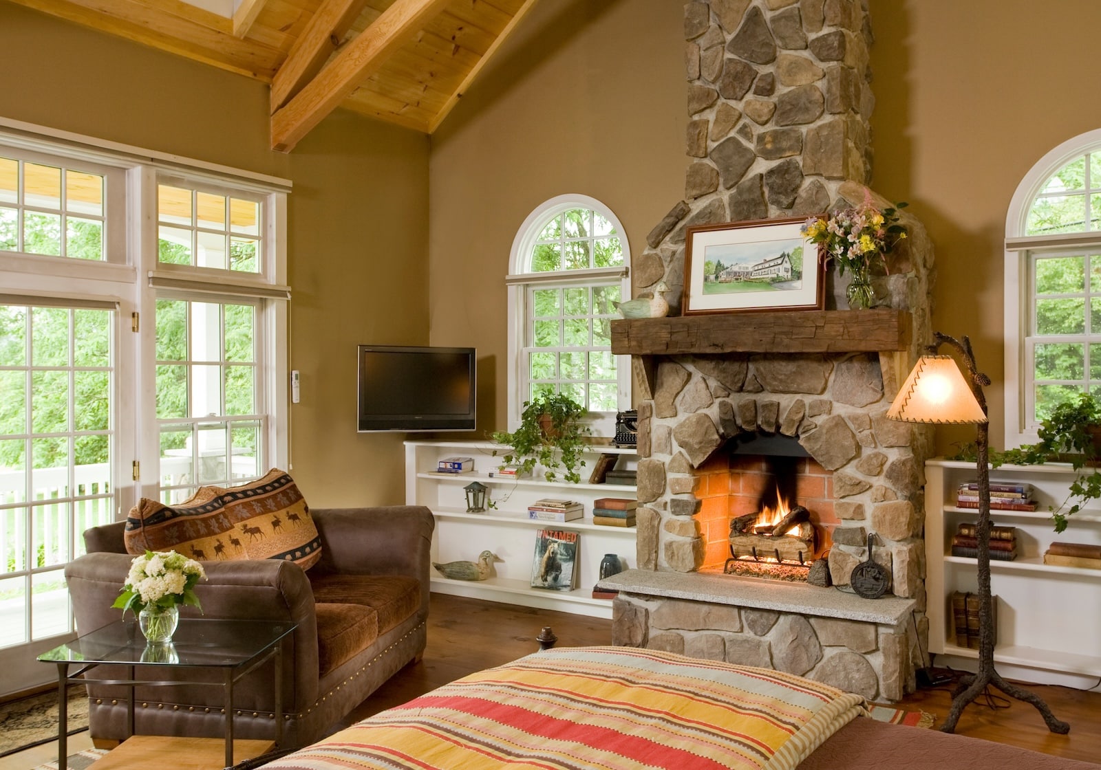 A room with a fire place surrounded by a TV, couch, lamp, and windows at the best New Hampshire Bed and Breakfast.
