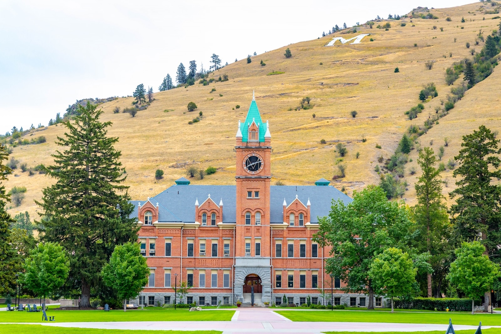 University Hall, a brick building with a mountain backdrop, at the University of Montana, near lodging near the University of Montana.