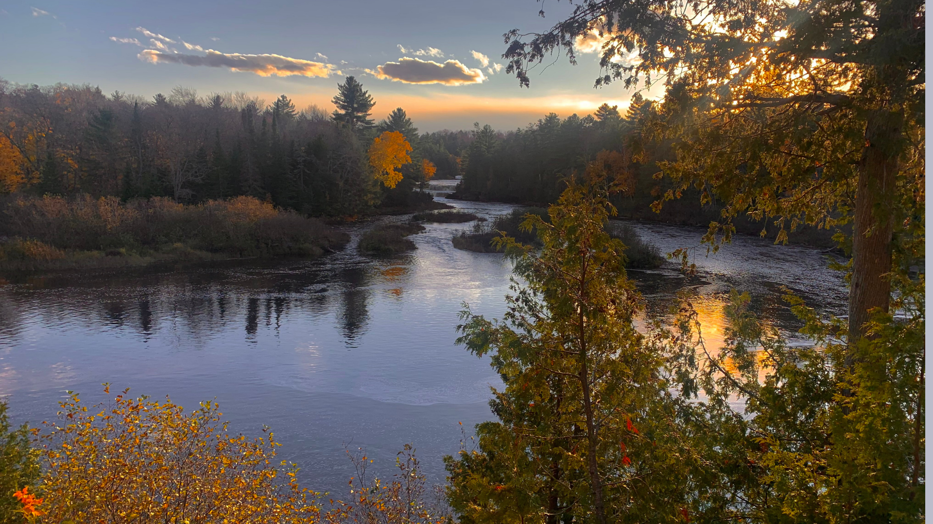 Peaceful autumn river landscape at sunset, with colorful trees lining the winding water and golden sunlight reflecting on the river.