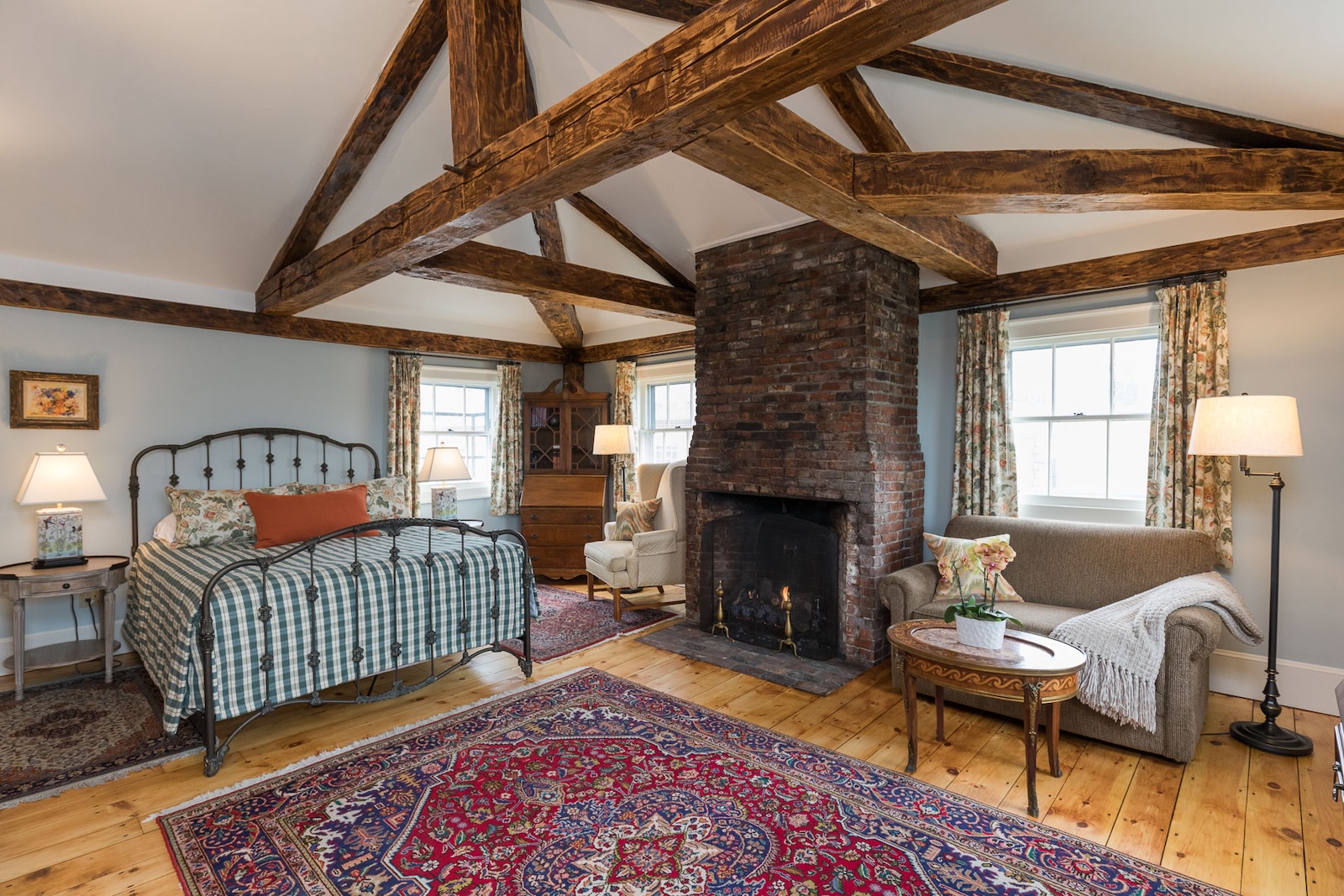 A room with a queen sized bed beside a table and lap, a sitting area and a brick fireplace at one of the best Exeter hotels.