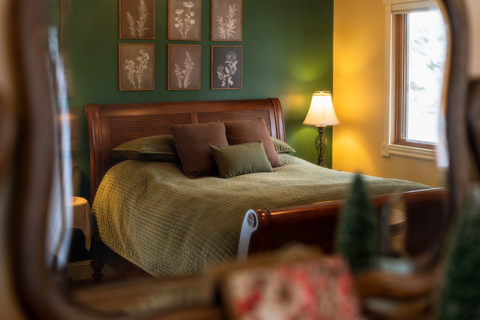 A bed in a green room by a window and lamp with art above the headboard at a Montana Bed and Breakfast.