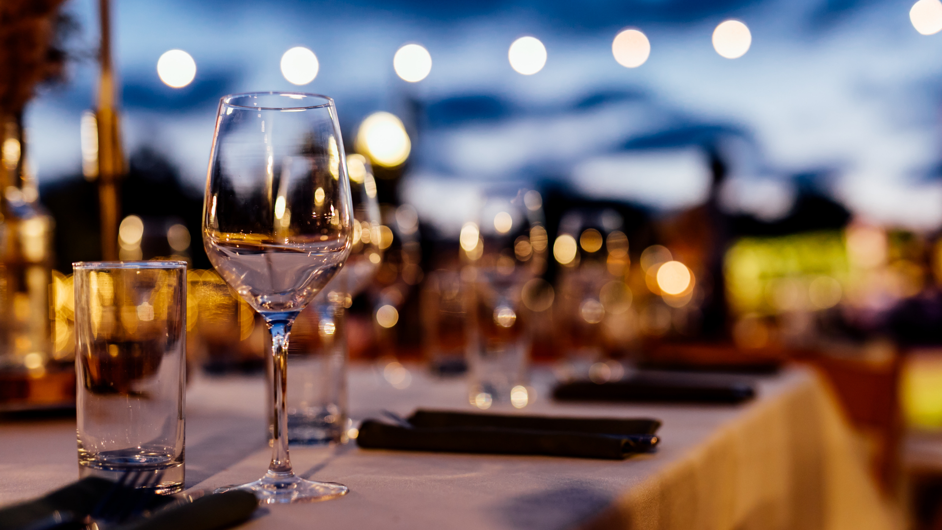 Elegant restaurant table setting with wine and water glasses, softly illuminated by warm evening lights.