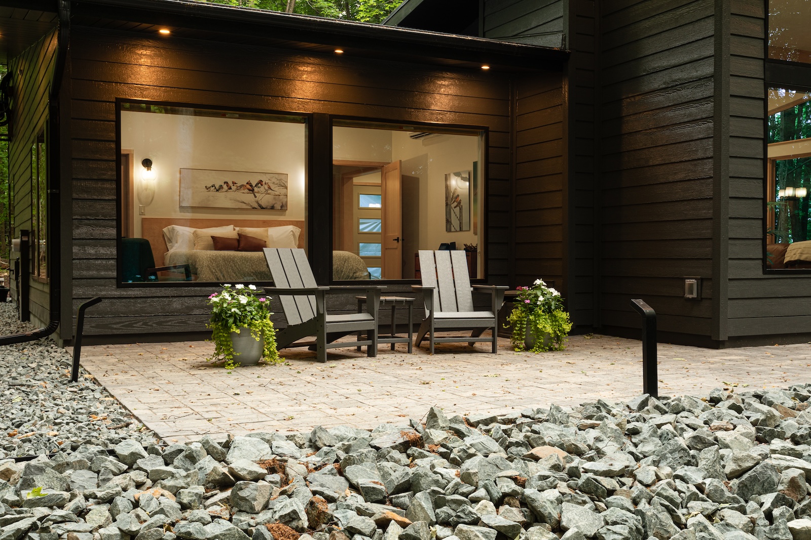 Two Adirondack chairs on a patio with large windows showcasing a bedroom in the background at one of the best Wisconsin cabin rentals.