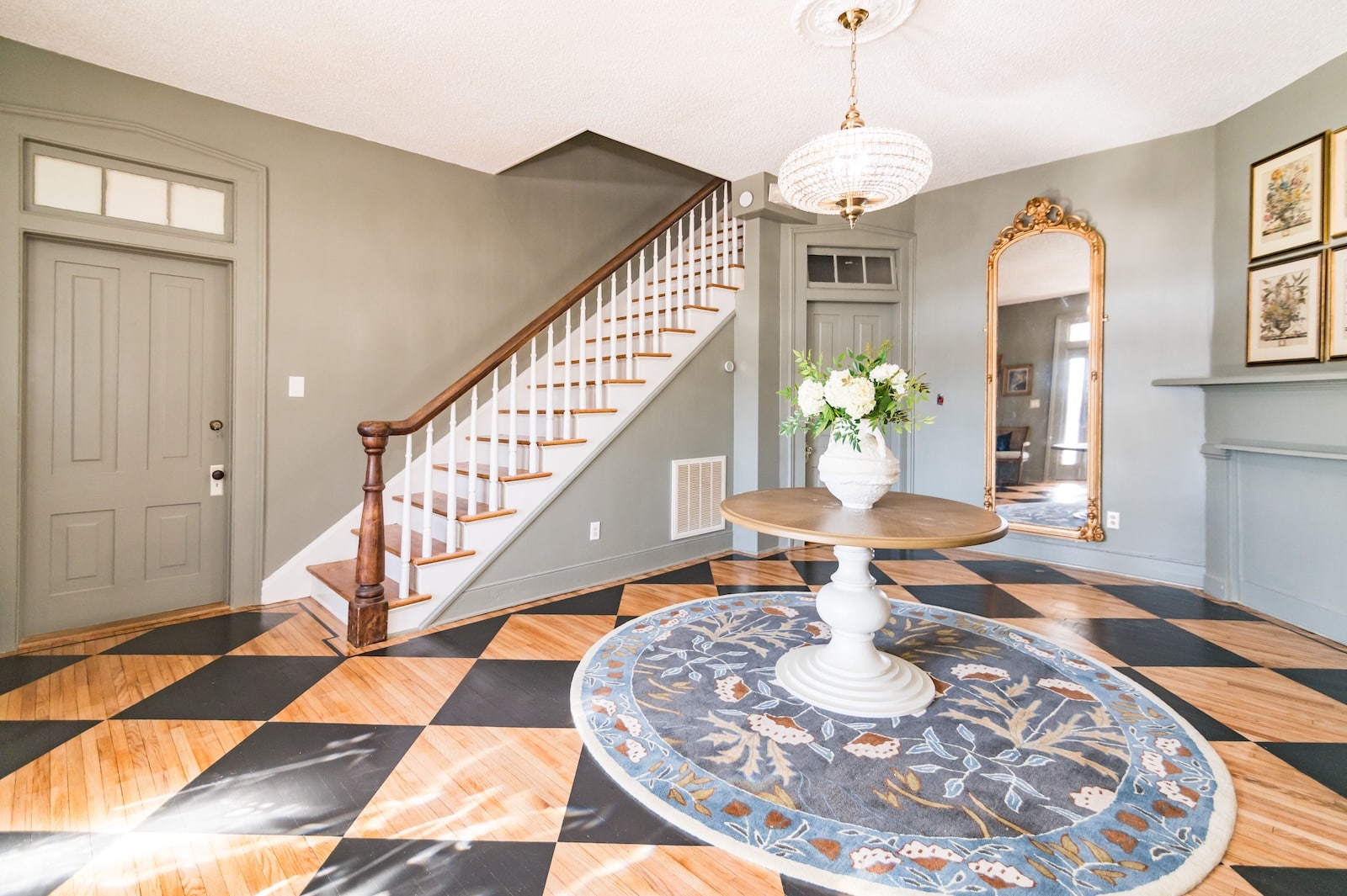 The parlor of the Orchard House, a bed and breakfast near Charlottesville VA, featuring a staircase, beautiful painted floors, a table with flowers, and a floor to ceiling mirror.