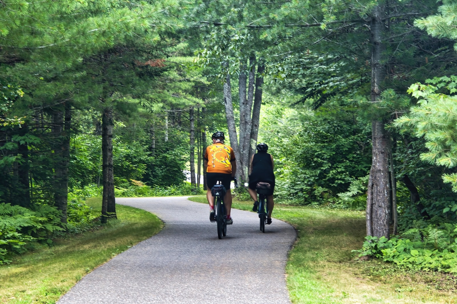 A man and woman riding bikes on a path with trees surrounding them on the Mountain Bay State Trail in Wausau, Wisconsin.