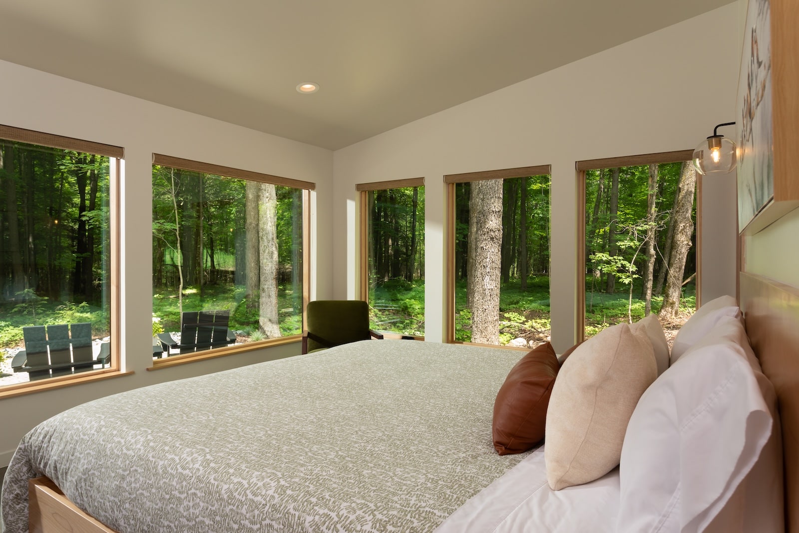 A bedroom with large widows showcasing surrounding wood as one of the most romantic secluded cabins in Wisconsin.