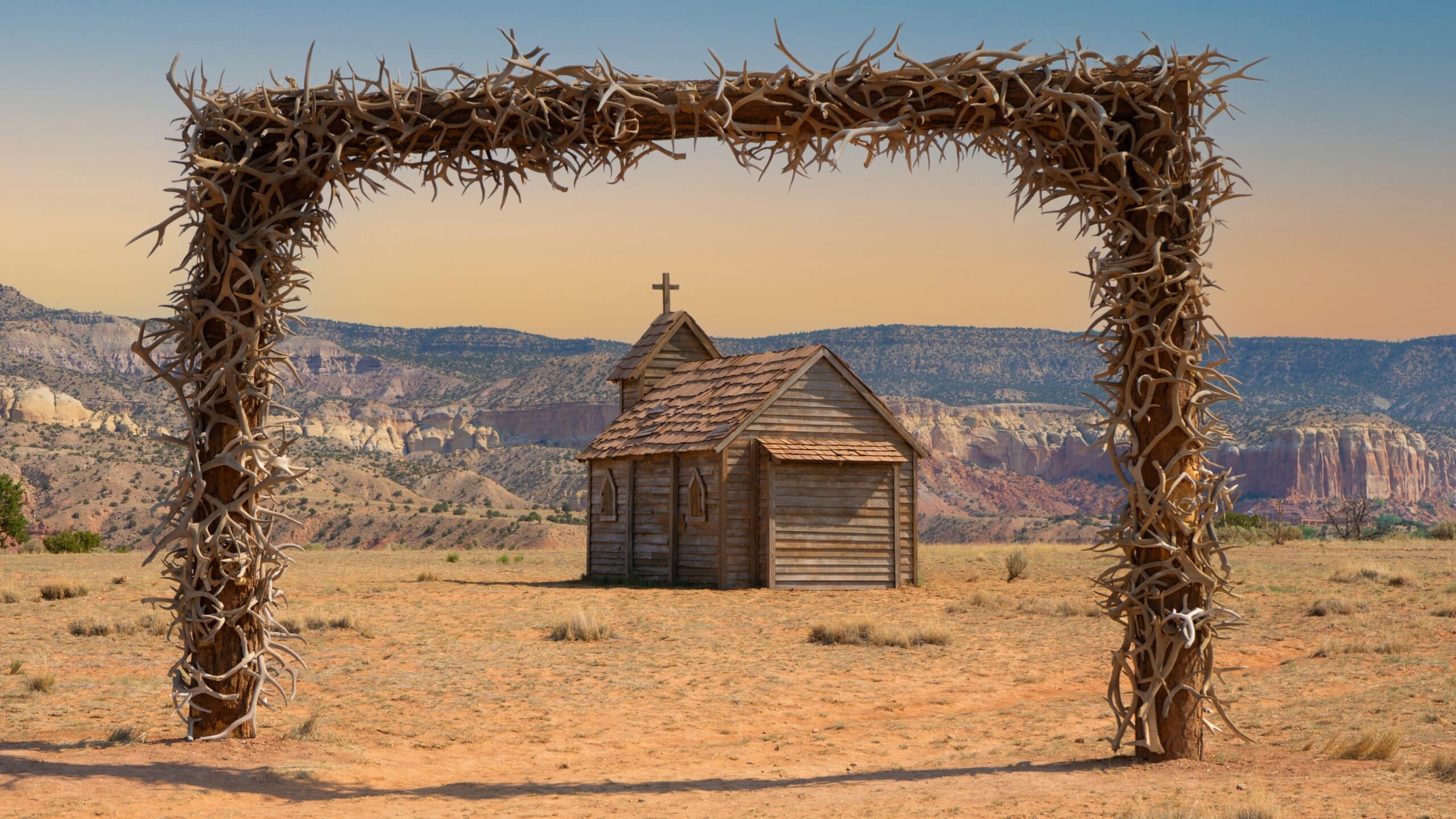 A wooden building in a field with an arch of antlers and a mountain view at Ghost Ranch in New Mexico.