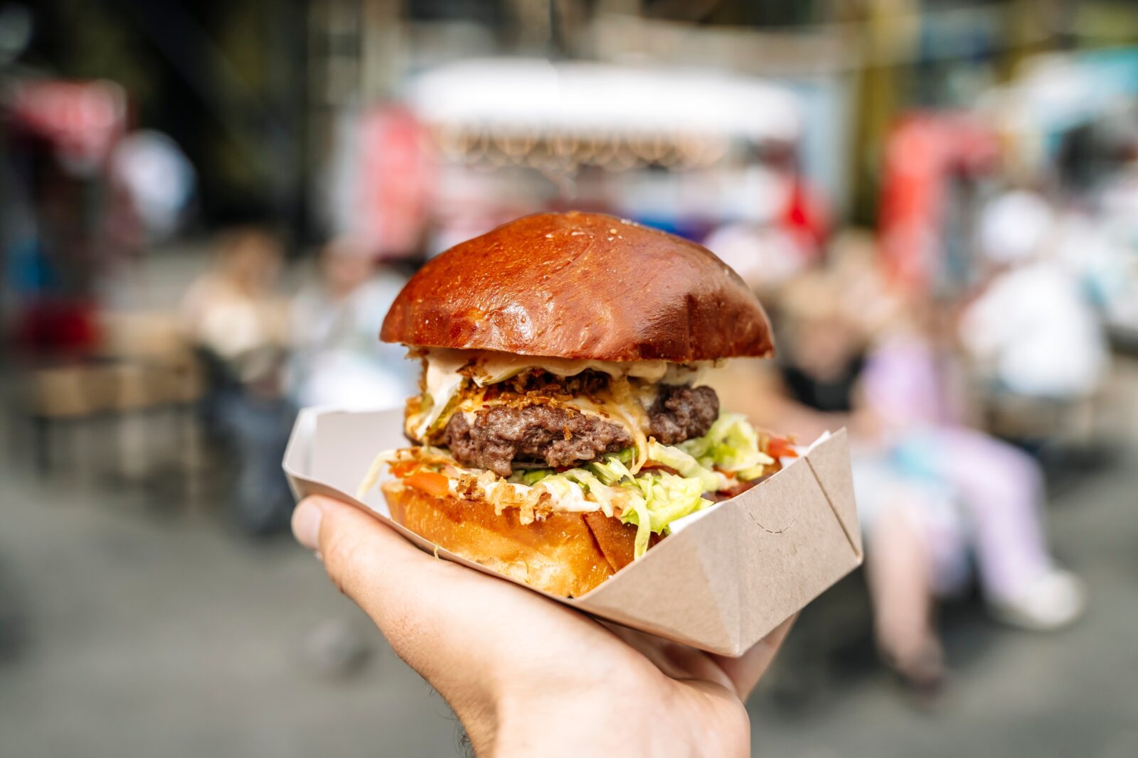Hand holds burger in craft paper boat, ordered from food truck at Bent Paddle Brewing