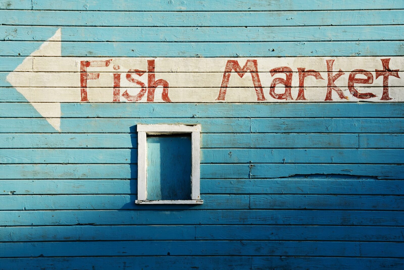 Blue building with white arrow, lettering in red paint reads "fish market" in Old Town Bandon Oregon
