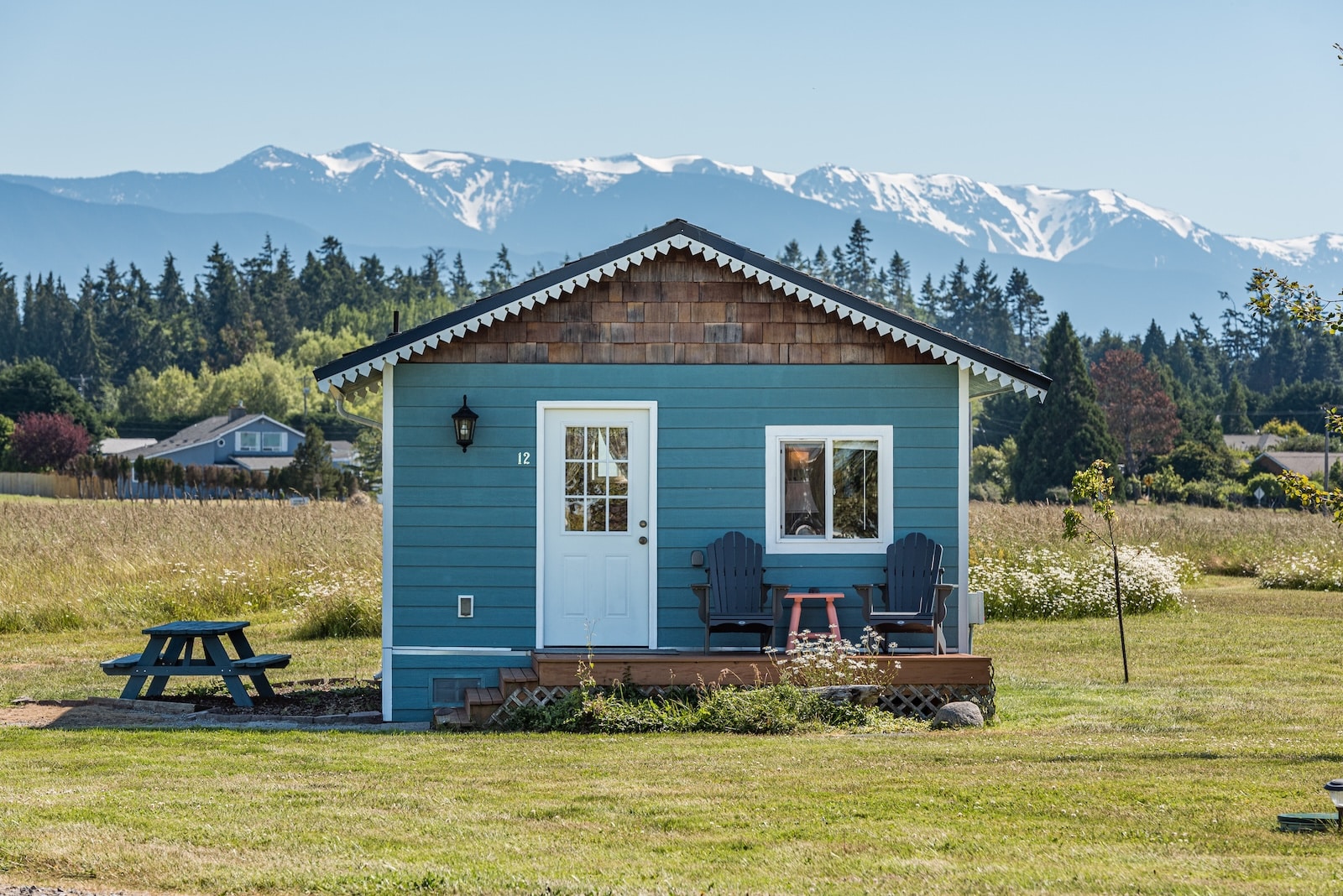 The Honeymoon Cottage, premier lodging among Sequim cottages, with a blue exterior and mountains in the background, great for anniversary getaway ideas.