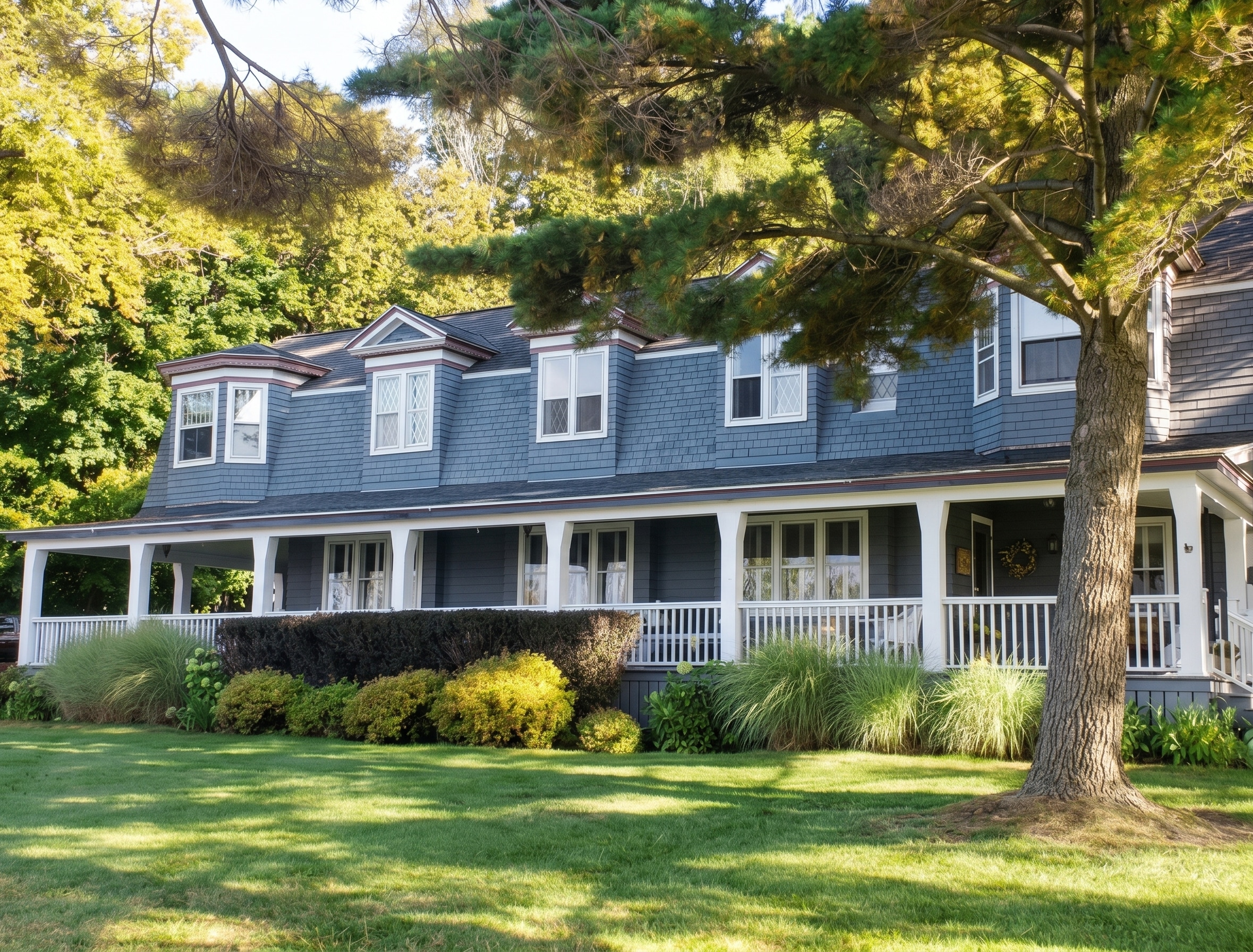 Canfield House: a large blue-shingled house with white trim and a long wraparound porch sits beneath mature trees, surrounded by a sunny, well-kept lawn.