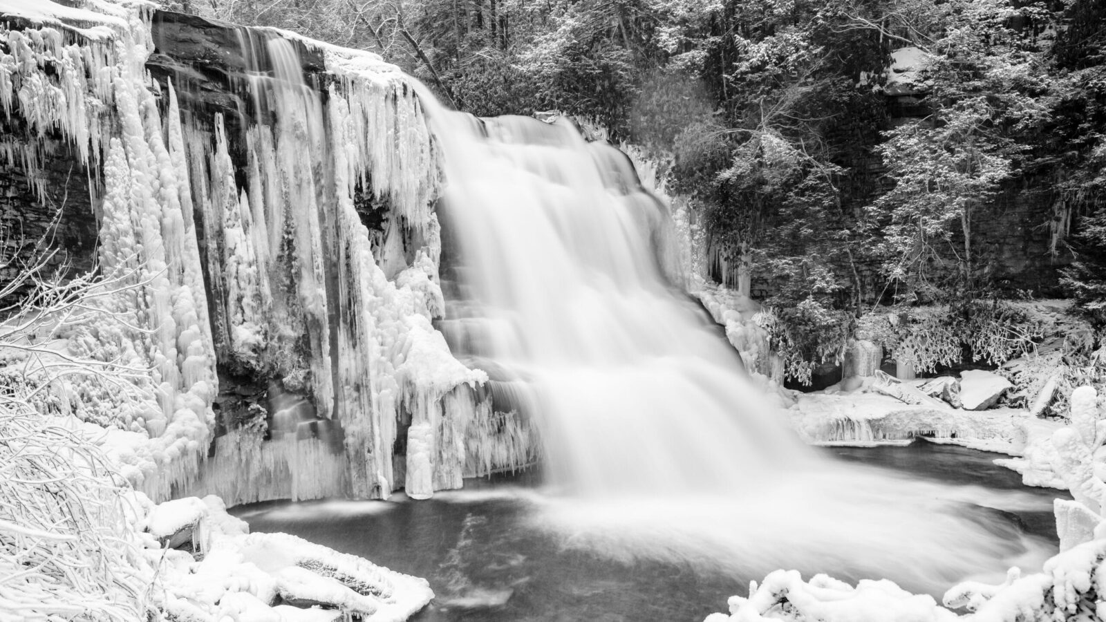 Muddy Creek Falls. The massive water movement of this stunning water fall contrasts with the frozen landscape surrounding it. Snowshoeing to the frozen waterfall is one of the most popular deep creek lake winter activities.