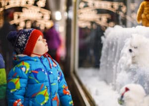 Adorable child bundled up in winter coat and hat looks at Christmas displays at Koziar's Christmas Village.