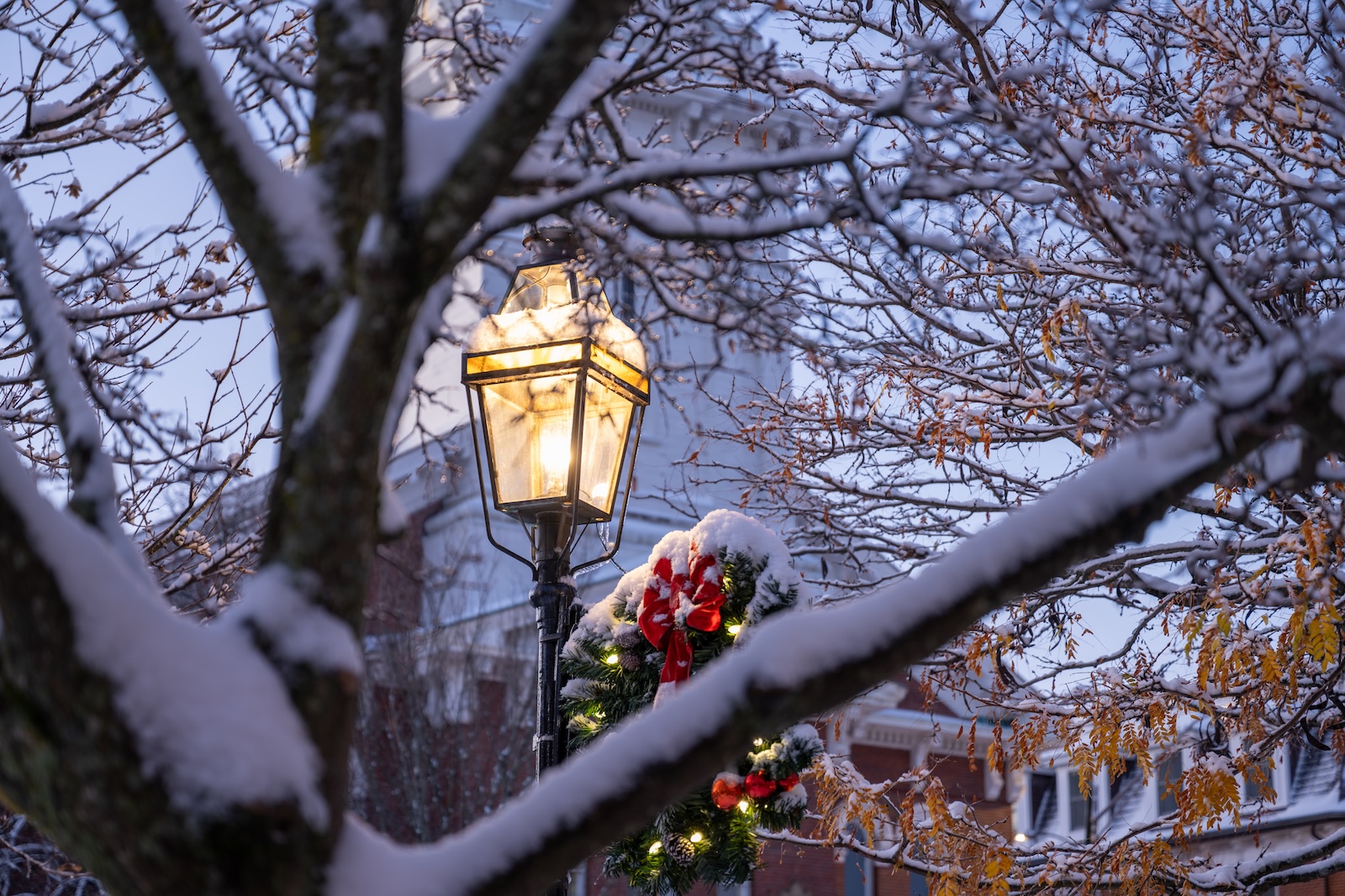 A wreath on a light with snow on the trees in Portsmouth, one of the best places to spend Christmas in New Hampshire.